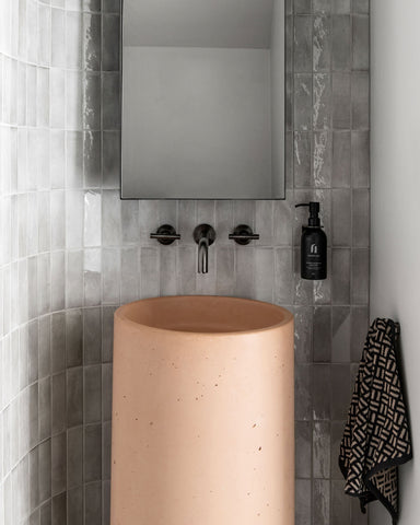 Luna Concrete pedestal basin in Pastel Peach sitting on grey and peach terrazzo tiles against a curved tiled wall with floor to ceiling Spanish Handmade Subway tiles in Grey with gunmetal tapware.
