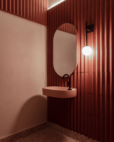 Spacious bathroom showcasing a blush pink Shelf Oval Wall Hung basin against a backdrop of red brick walls, complemented by a terrazzo floor and sleek black tapware.