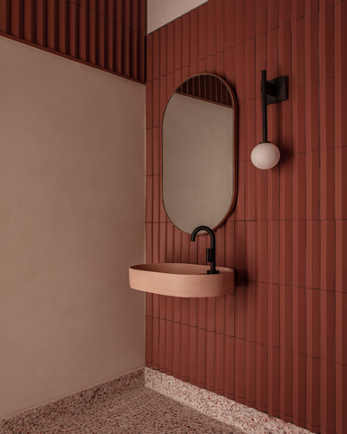 Modern bathroom with a standout blush pink Shelf Oval Wall Hung basin, set against red brick walls, anchored by a terrazzo floor, and accented with contemporary black tapware.