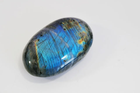 An iridescent labradorite stone with shades of blue, green, and gold, resting on a black surface.