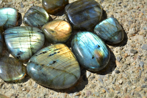 An iridescent labradorite stone with shades of blue, green, and gold, resting on a black surface.