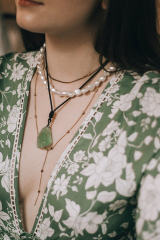 Gros plan sur le cou d'une femme portant un collier de pierres précieuses vertes, le pendentif reposant sur sa poitrine.