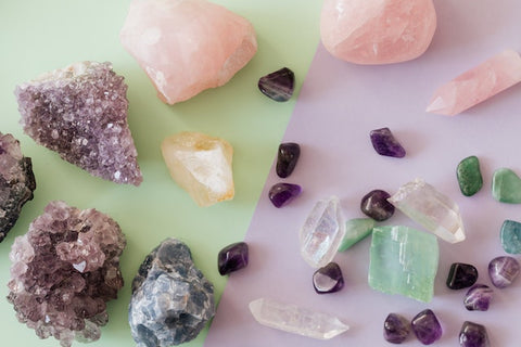 Gros plan de pierres précieuses de quartz rose et d'améthyste disposées sur une surface blanche, mettant en valeur leurs couleurs et textures naturelles.