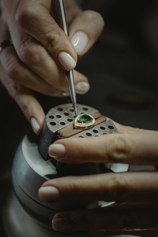 Un groupe d'artisans qualifiés assis à un établi, travaillant méticuleusement sur des bijoux fins en utilisant divers outils et techniques, avec des loupes et des lumières vives pour les aider dans leur travail.
