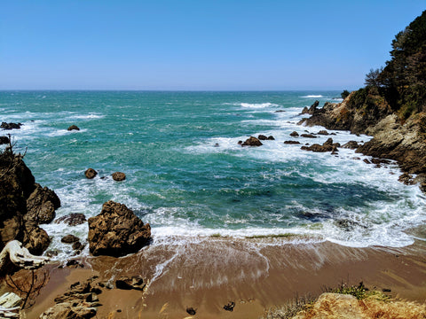 Waves crashing against brown rocks, in a cove, blue sky without clouds, blue water