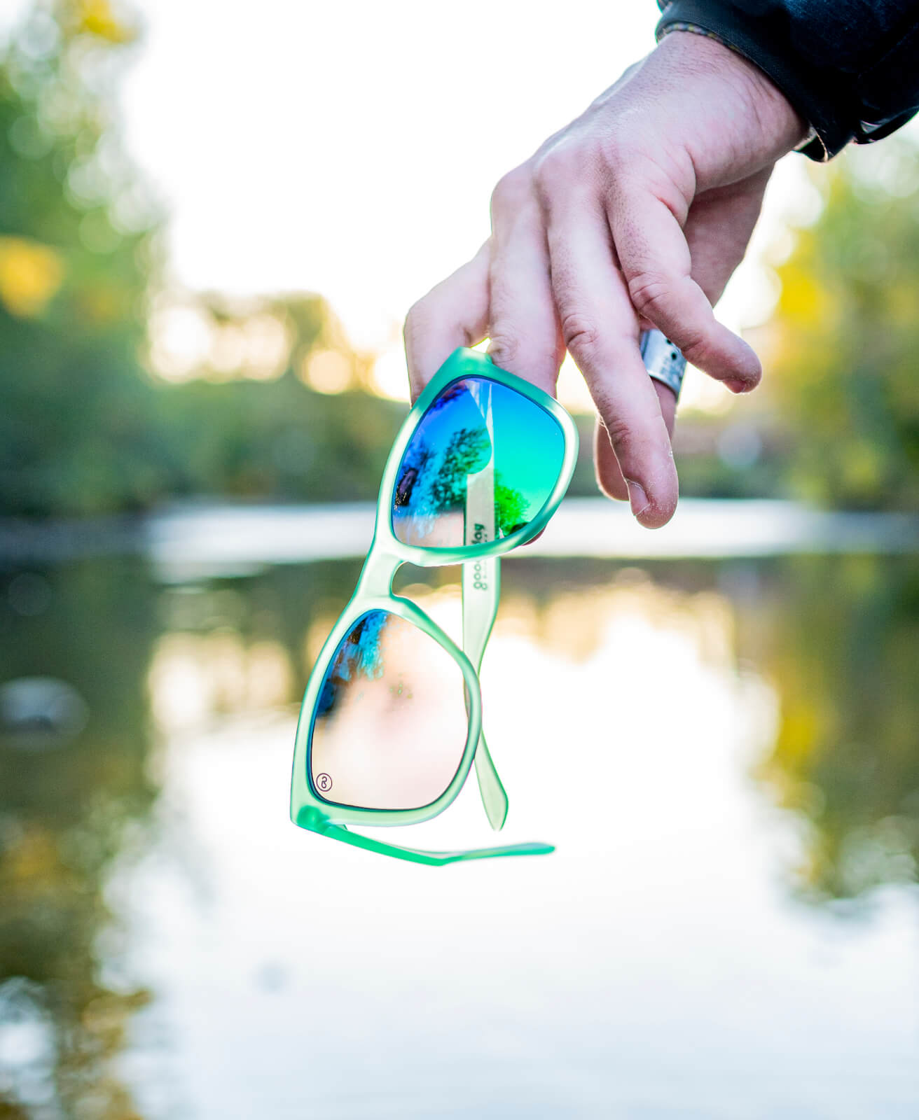 a pair of green sunglasses held in hand by a river