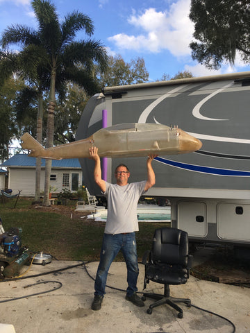 Man holding up shell of fiberglass blackhawk helicopter standing in front of an RV.