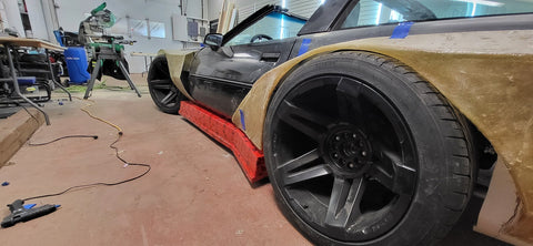 Side view of fiberglass and resin customization on side of black corvette sitting in a garage with cutting tools nearby.