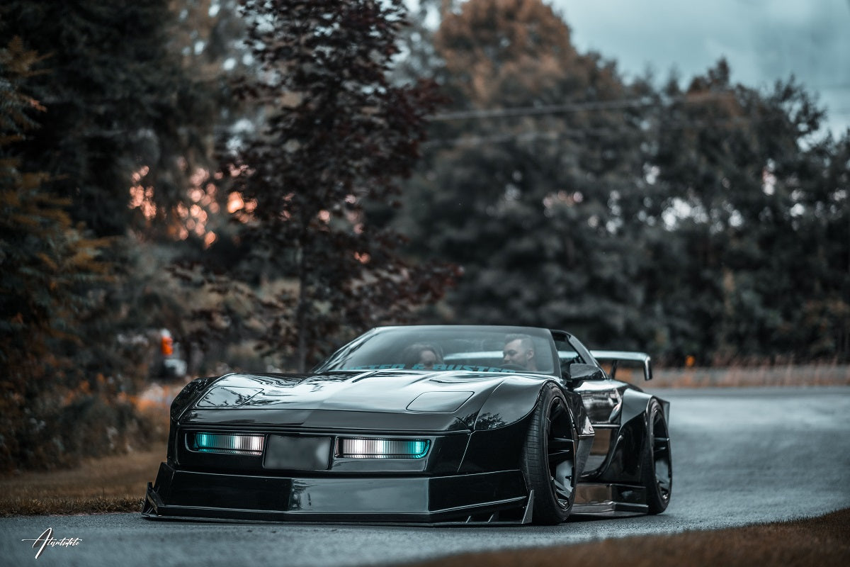 Black Custom Corvette driving on road with a man and a woman inside.