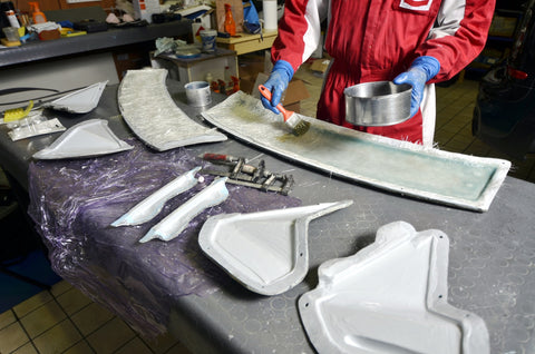 man in safety suit adding chopped strand mat evenly with resin to a mold