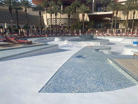 Large hotel pool recently resurfaced surrounded with lounge chairs and palm trees.