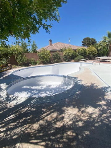 Empty swimming pool and hot tub newly resurfaced with white gelcoat and blue tiles.