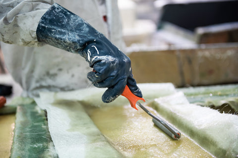 person in safety clothing rolling polyester resin into chopped strand mat with fiberglass roller