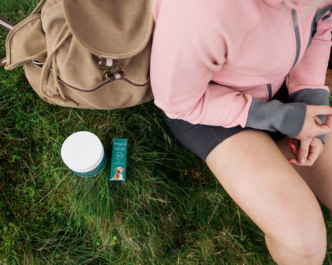 lady sat outside with CBD oil and topical balm on the grass