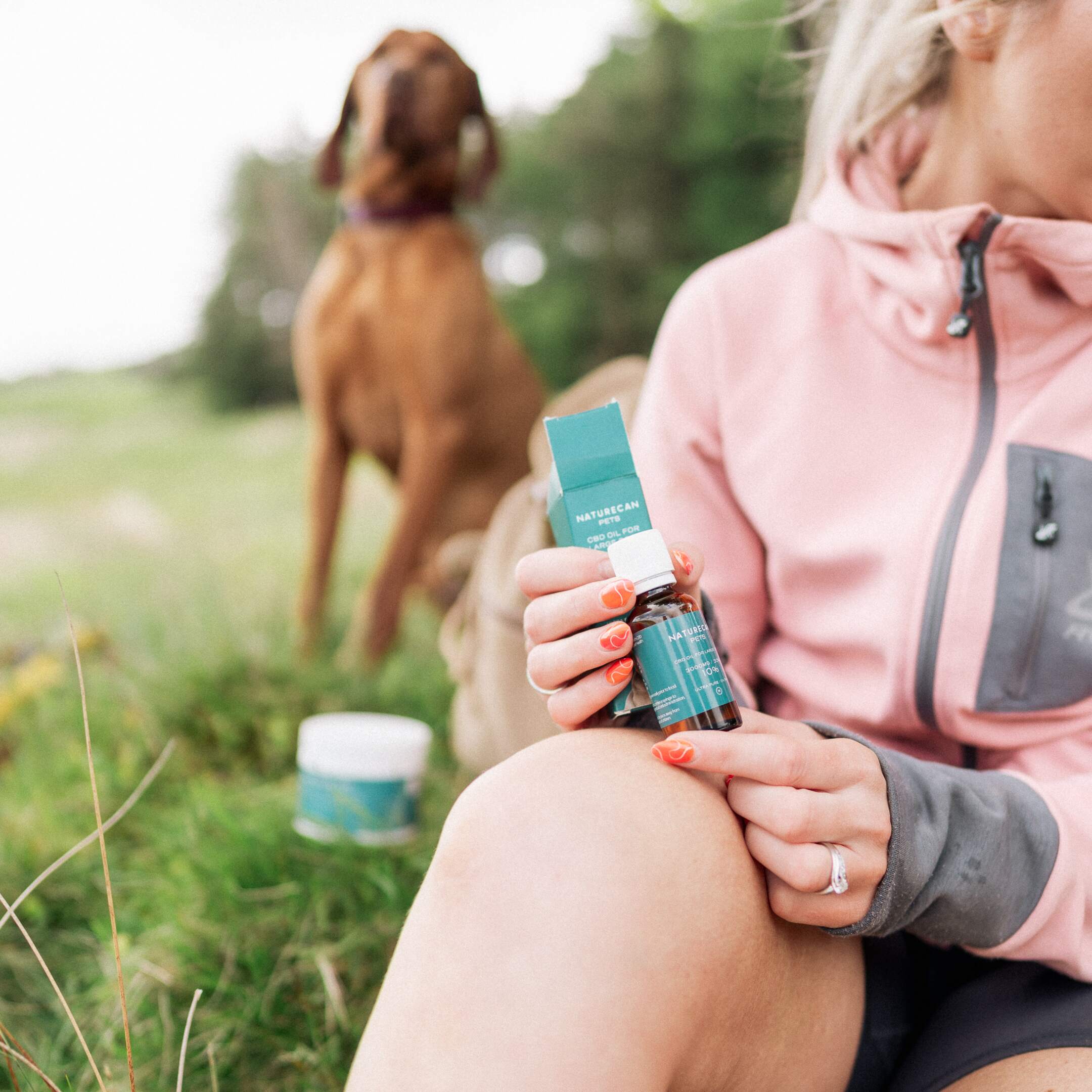lady holding our CBD oil in a field with her dog in the background lady holding our CBD oil in a field with her dog in the background