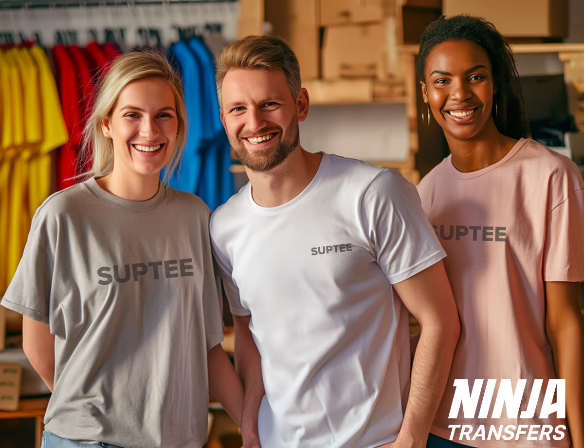 Smiling successful T-shirt business owner posing with their small team, with various printed t-shirts hanging from a rack and boxes stacked nearby.