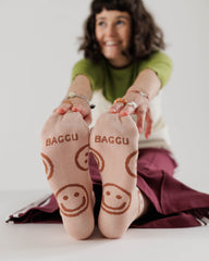 a smiling woman sitting on the floor reaching to her toes showing aa peach coloured pair of socks with vintage happy faces on them in a darker colour 
