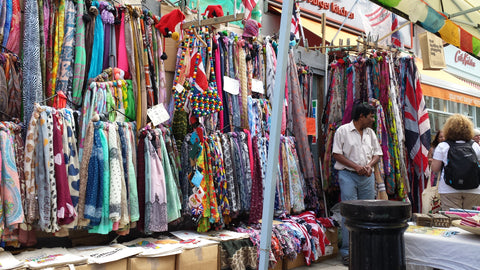 Shop front on Portobello Road with hundreds of clothes and fabrics draped chaotically outside, whilst Rushab's dad tends to the display