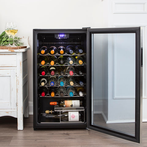 A black wine fridge sits on the floor next to a white table. The wine fridge is completely filled with bottles.