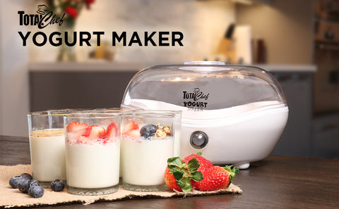 A white yogurt maker sits on a brown table. In front of it, are four glasses of yogurt, one is filled with strawberries and one is filled with blueberries and granola. In the top left corner is text reading "Total Chef" with a chef hat and "Yogurt Maker".