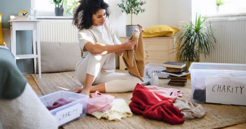 Picture of a person with light skin and curly brown hair wearing white leggings and t-shirt sitting on the floor and sorting things into boxes labeled 