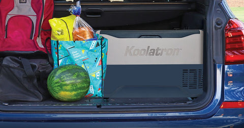 Closeup picture of a Koolatron SmartKool 12 volt travel freezer in the trunk of a blue SUV with a duffle bag, backpack, grocery bag, and watermelon beside it