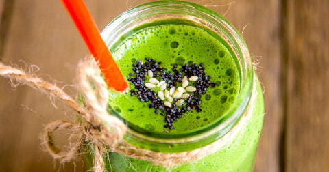 Closeup image of a glass jar filled with bright green smoothie with sesame and poppyseeds arranged in a heart shape on top