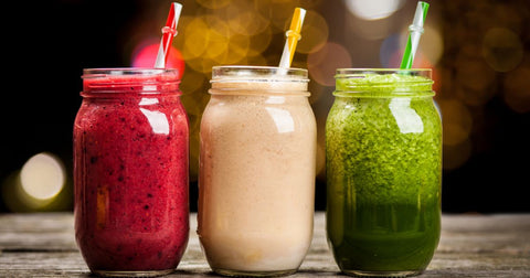 Photo of three mason jars containing a purple-red berry smoothie, a cream-coloured almond-peach smoothie, and a bright green smoothie with matching straws