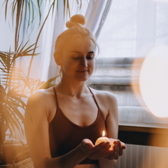 woman holding a candle has her eyes closed and is meditating