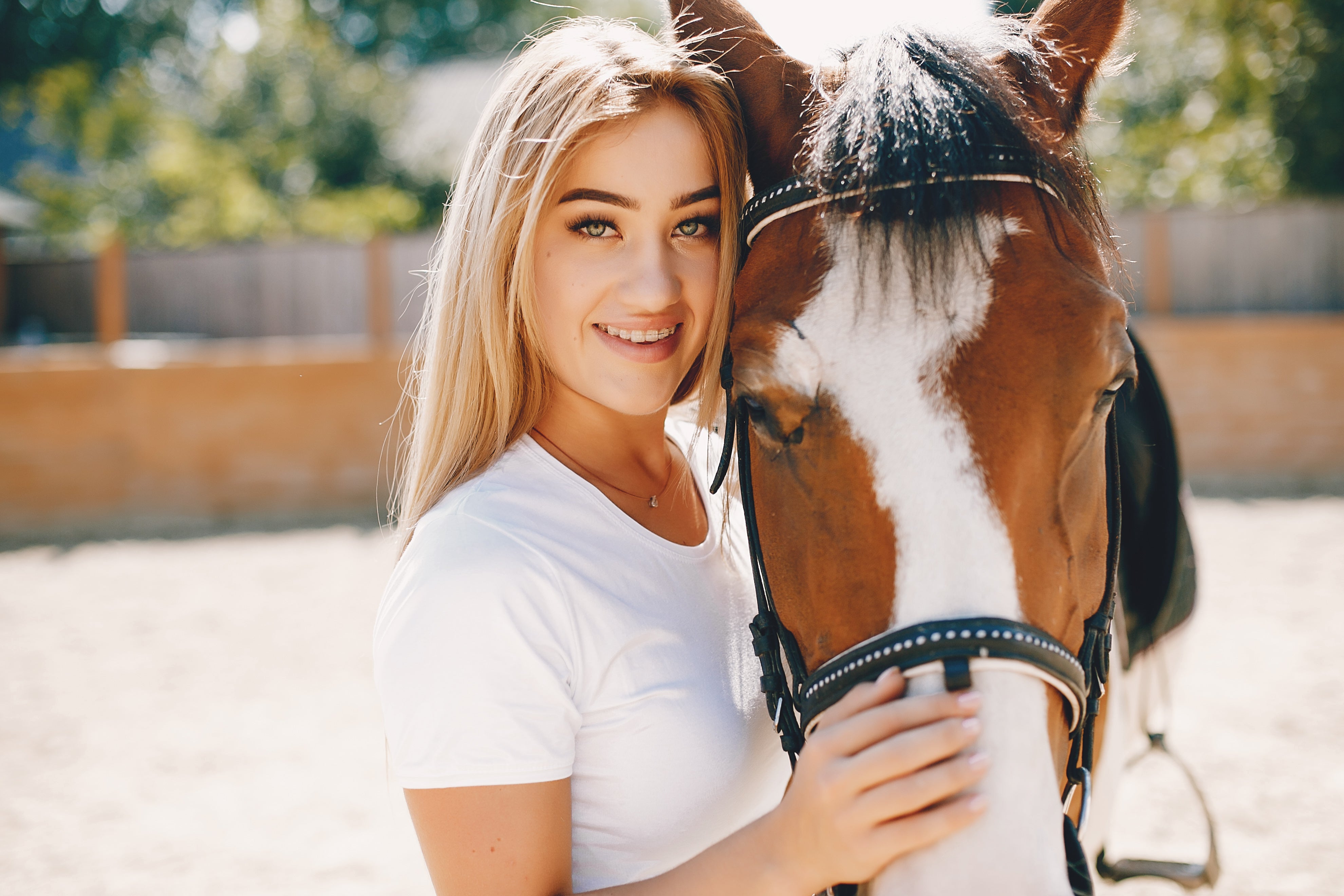 Foto einer lächelnden Frau, die liebevoll neben einem Pferd steht und direkt in die Kamera blickt, symbolisiert die harmonische Beziehung zwischen Mensch und Tier, ideal für eine Webseite, die sich auf Produkte und Dienstleistungen für Pferde und ihre Besitzer spezialisiert hat.