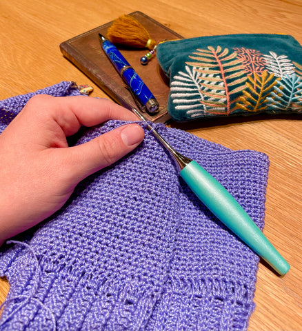 Kelly's crochet design in progress: hands and a crochet hook with a swatch of a sweater