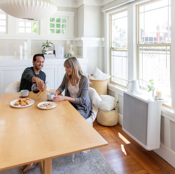 Two friends have coffee at a table next to a window heat pump