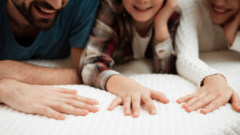 family of 3 testing a mattress by laying on it and pressing down to test the firmness