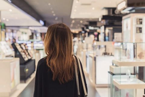 A women is walking through a luxury retail store while looking around. The photo is taken from the back from the waist up.