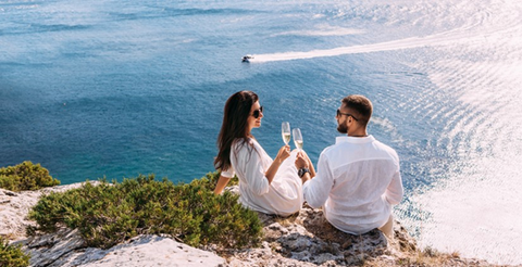 Conclusion - A young couple is sitting on a cliff overlooking the ocean while the sun sets.