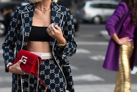 A women in Gucci jumpsuit is holding a red Gucci handbag on the street.