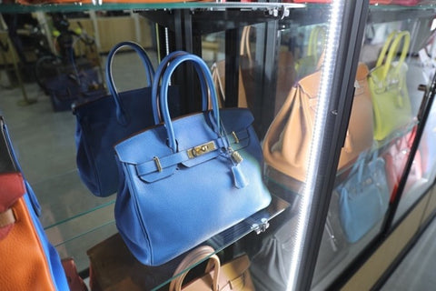 A royal blue Hermès Birken bag sits in a display case.