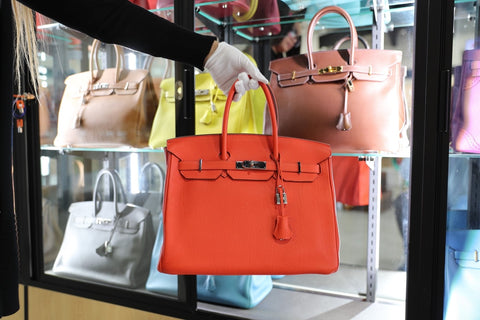 A Max Pawn Team Member is holding an orange Hermès Birkin bag.