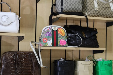 A collection of luxury handbags are displayed on the wall. A Gucci bag is front and center.