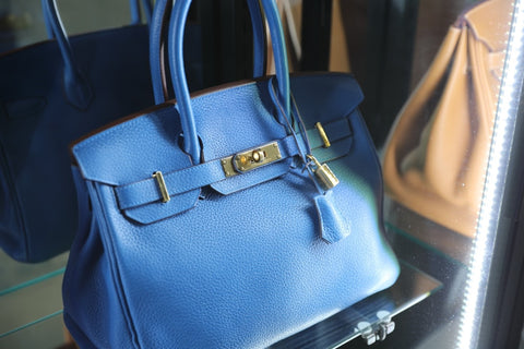 A blue Hermès Birkin bag sits inside a display case.