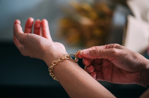 A women is putting on a gold chain on her wrist.