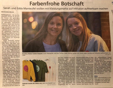 Ein Zeitungsartikel mit einem großen Foto von Sarah und Edda. Sie stehen nebeneinander und lachen in die Kamera. Beide haben lange braune Harre, die sie offen tragen. Der Titel lautet "Farbenfrohe Botschaft" Darunter steht "Sarah und Edda Manteufel wollen mit Kleidungsmarke auf Inklusion aufmerksam machen". Der Artikel ist online verfügbar, der link ist im Blogbeitrag verlinkt.