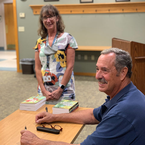 Jeff Nania sitting at a table smiling with Reedsburg librarian standing in the background