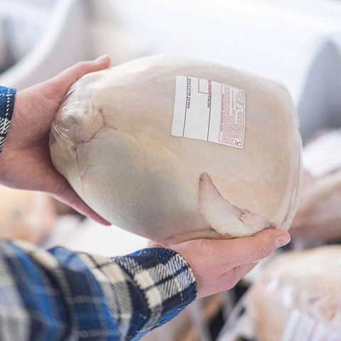 a person holding a wrapped and labeled whole chicken