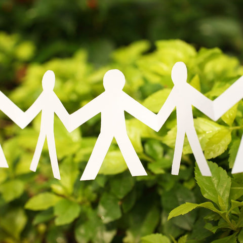 people holding hands cut out of paper in front of green plants