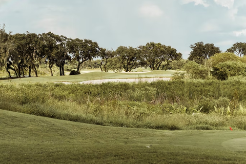 A view from the rough across a bunker and onto the green