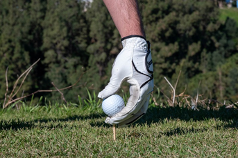 A left-handed golf glove placing a ball on the tee