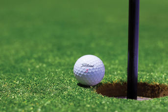 A golf ball teetering on the brink of a hole