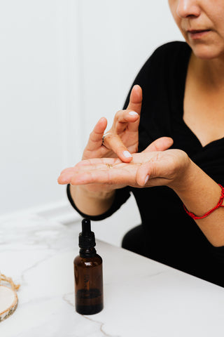 A woman with a bottle of hair growth oil, she's putting some in her palm to apply.
