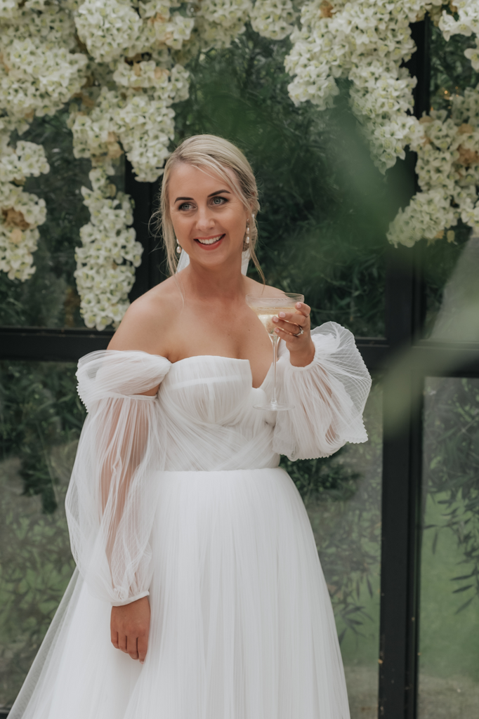 Bride wears off-the-shoulder dress with sleeves.